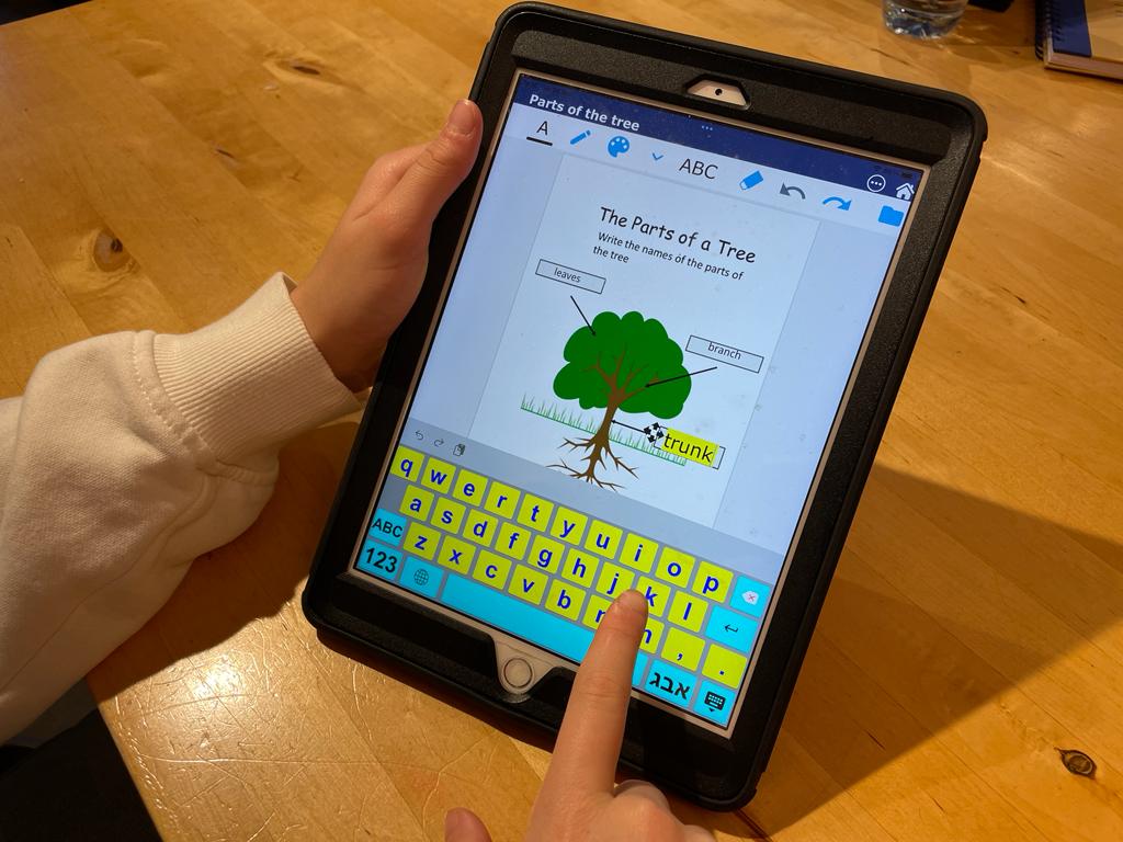 ipad on table with IssieDocs open. worksheet with image of tree. see two hands in ohoto, one holding ipad and other typing on keyboard.